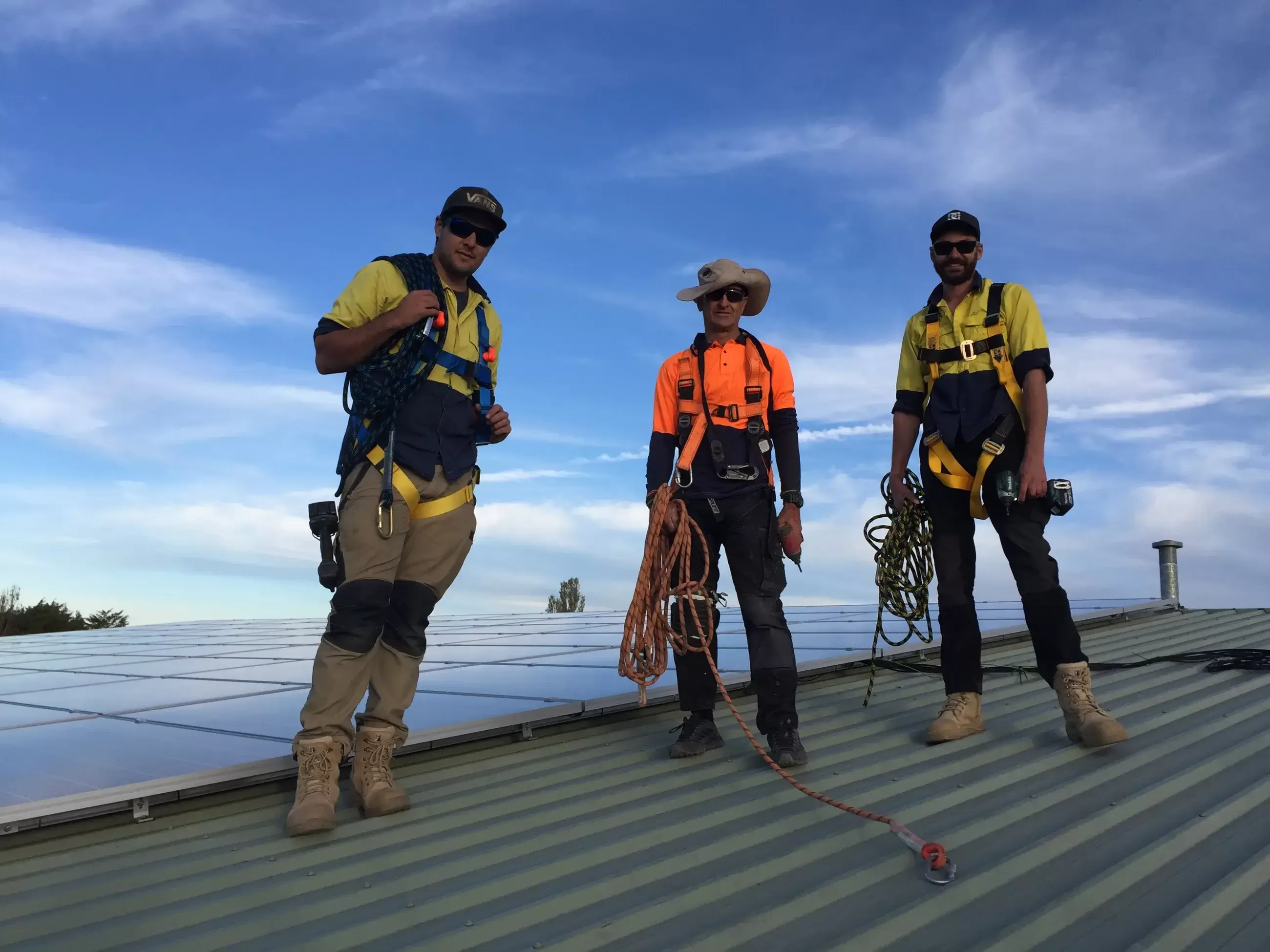 Three solar installers standing safely on a rooftop